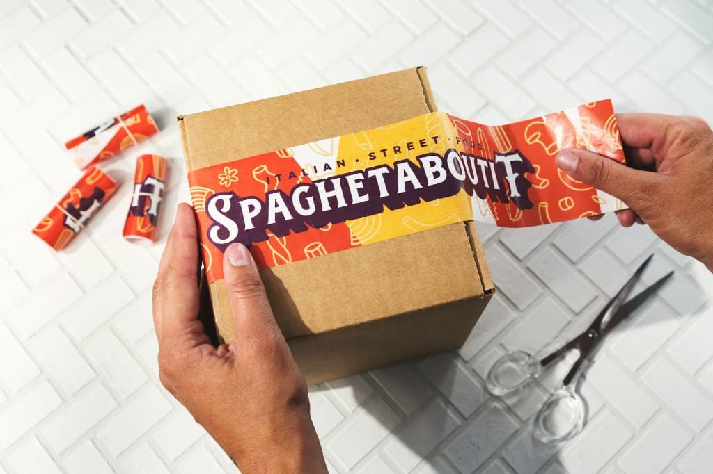 Hands unboxing a custom-branded Spaghetabout It shipping carton.
